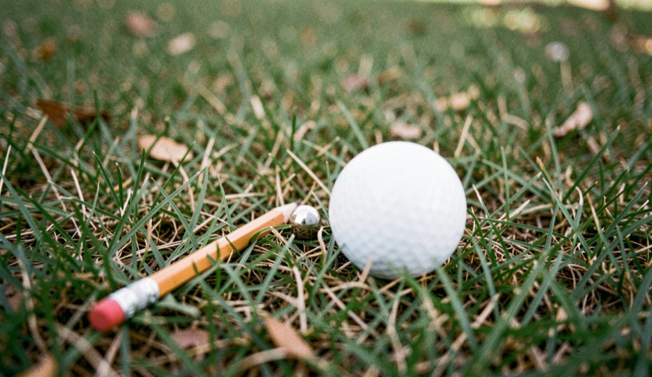Kort potlood en een metalen merker liggen in het kortgemaaide gras naast een witte golfbal